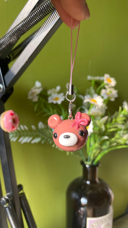 Bear Charm polymer clay charm, in-hand scale showing glossy brown bear face with pink bow and white muzzle