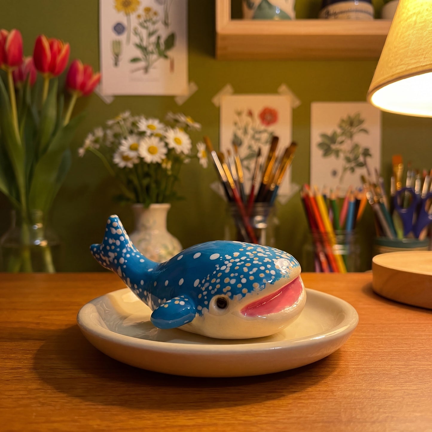 Happy Whale handmade glossy clay desk pal, in the Moon Kiln studio, evening lamp light