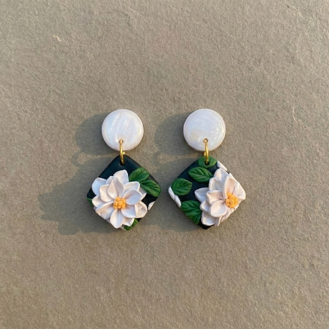 White Lotus handmade polymer-clay earrings, the pair on a warm stone surface
