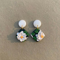 White Lotus handmade polymer-clay earrings, the pair on a warm stone surface