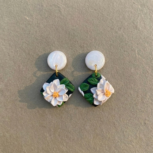 White Lotus handmade polymer-clay earrings, the pair on a warm stone surface