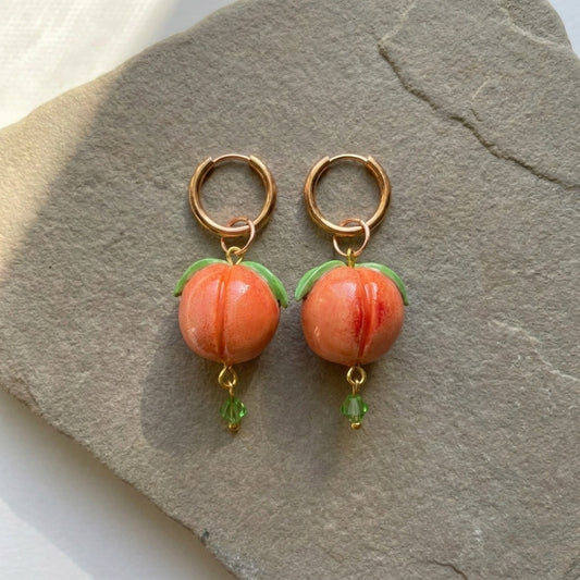 Peaches handmade polymer-clay earrings, the pair on a warm stone surface