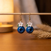 Blueberries handmade polymer-clay earrings, displayed on a stand in warm evening light