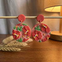 Hibiscus handmade polymer-clay earrings, displayed on a stand in warm evening light