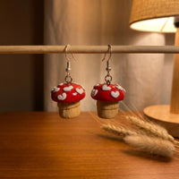 Shroom hearts handmade polymer-clay earrings, displayed on a stand in warm evening light