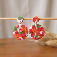 Frangipani handmade polymer-clay earrings, displayed on a stand in soft daylight