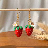 Strawberries handmade polymer-clay earrings, displayed on a stand in soft daylight