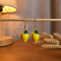Lemonita handmade polymer-clay earrings, displayed on a stand in warm evening light