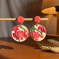 Pink Tipped Lotus handmade polymer-clay earrings, displayed on a stand in warm evening light