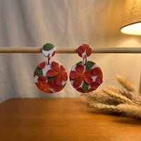 Frangipani handmade polymer-clay earrings, displayed on a stand in warm evening light