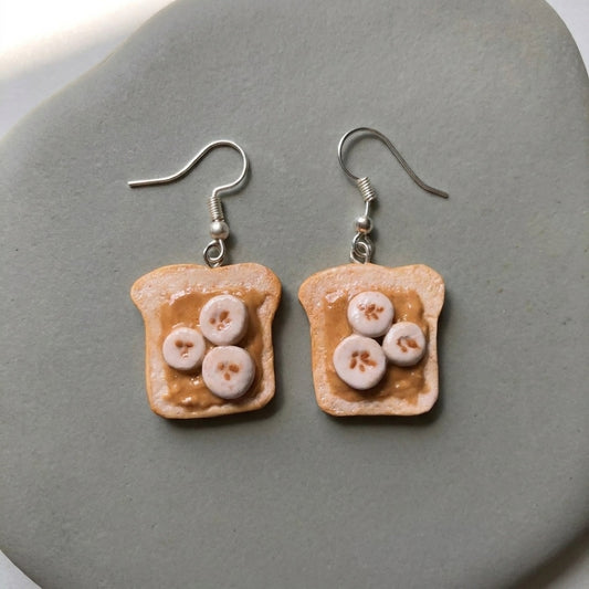 Peanut Butter and Banana earrings handmade polymer-clay earrings, the pair on a warm stone surface