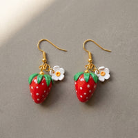 Strawberries handmade polymer-clay earrings, the pair on a warm stone surface