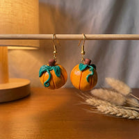 Pumpkiln handmade polymer-clay earrings, displayed on a stand in warm evening light