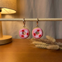 Donut Hearts handmade polymer-clay earrings, displayed on a stand in warm evening light