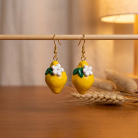 Lemonita handmade polymer-clay earrings, displayed on a stand in warm evening light