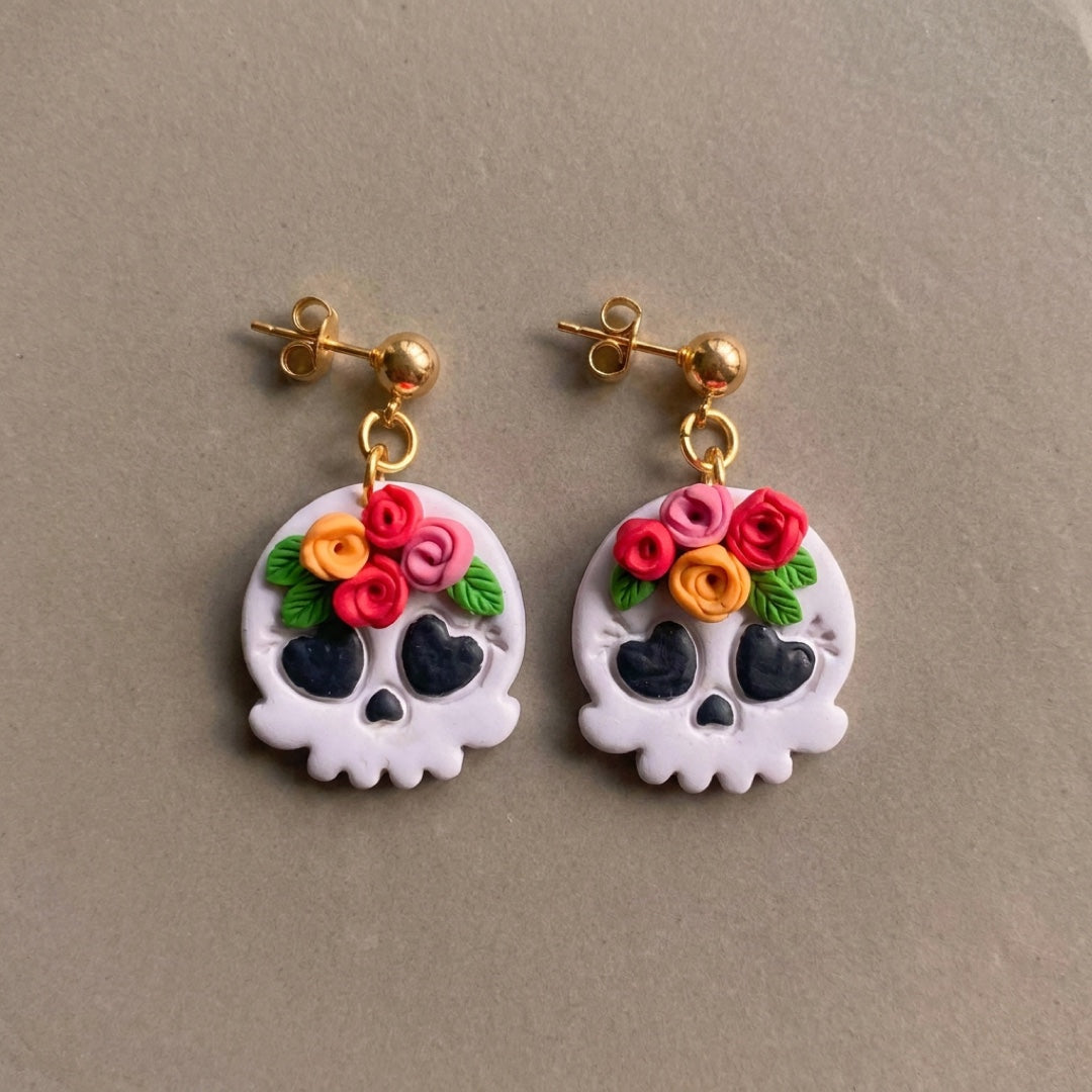 Skull and Flora handmade polymer-clay earrings, the pair on a warm stone surface