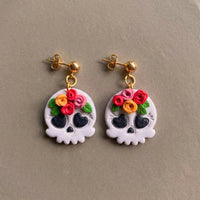 Skull and Flora handmade polymer-clay earrings, the pair on a warm stone surface
