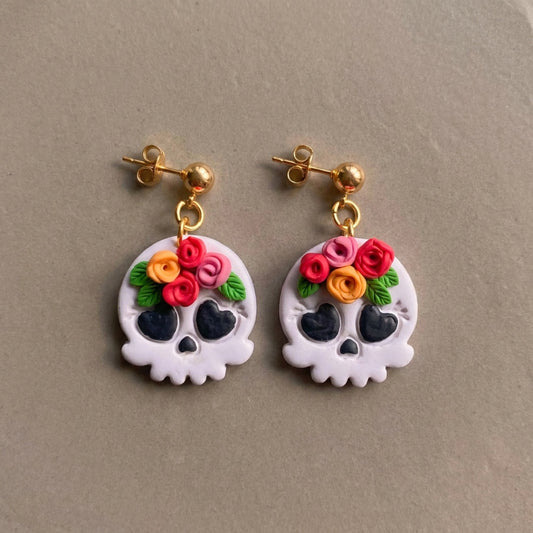 Skull and Flora handmade polymer-clay earrings, the pair on a warm stone surface