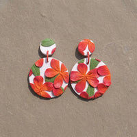 Frangipani handmade polymer-clay earrings, the pair on a warm stone surface