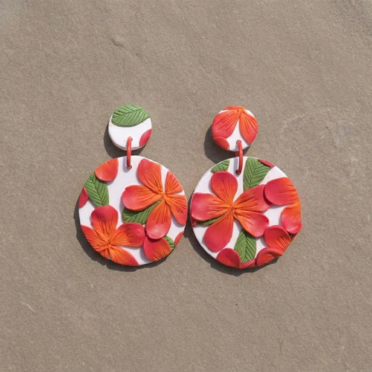 Frangipani handmade polymer-clay earrings, the pair on a warm stone surface