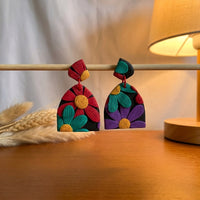Chroma Flora handmade polymer-clay earrings, displayed on a stand in warm evening light