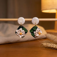 White Lotus handmade polymer-clay earrings, displayed on a stand in warm evening light