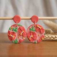 Hibiscus handmade polymer-clay earrings, displayed on a stand in soft daylight