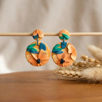 Tropical Daylily handmade polymer-clay earrings, displayed on a stand in soft daylight