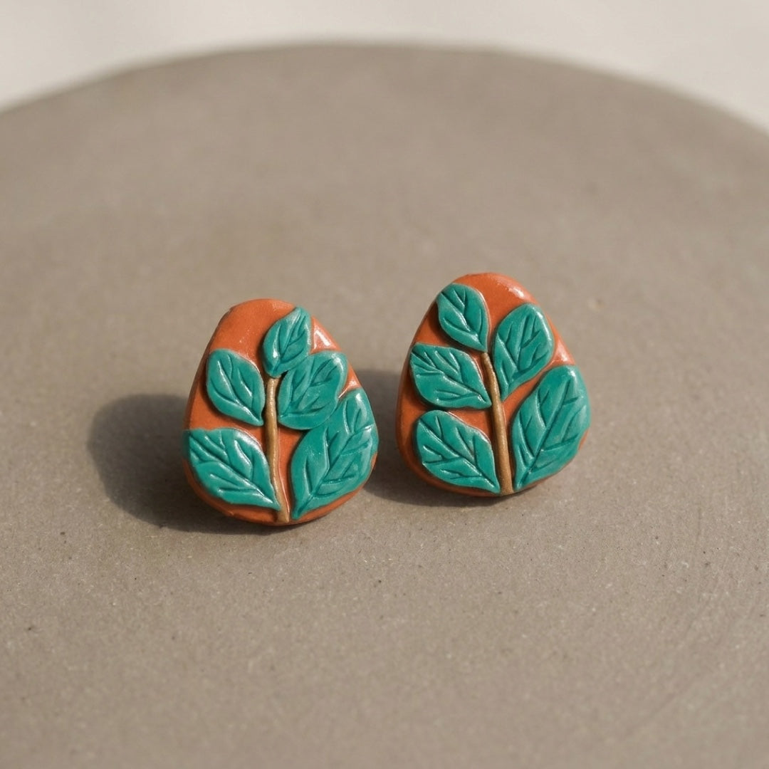 Leafy Studs handmade polymer-clay earrings, the pair on a warm stone surface