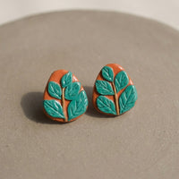 Leafy Studs handmade polymer-clay earrings, the pair on a warm stone surface
