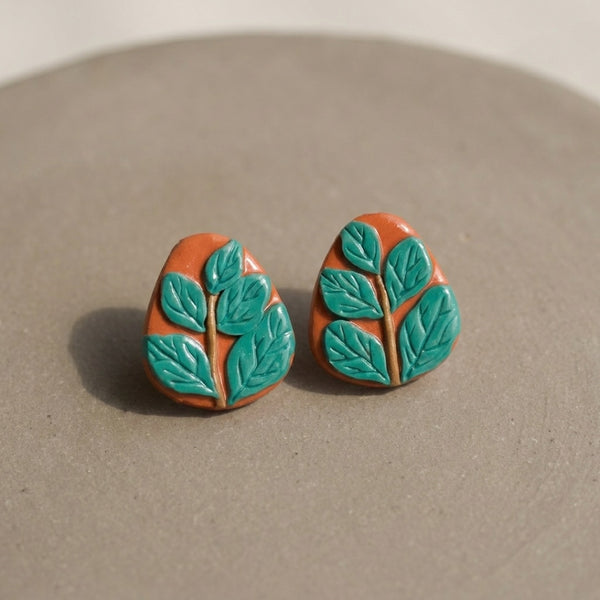 Leafy Studs handmade polymer-clay earrings, the pair on a warm stone surface