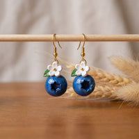 Blueberries handmade polymer-clay earrings, displayed on a stand in soft daylight