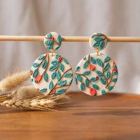 Teal Forest handmade polymer-clay earrings, displayed on a stand in soft daylight