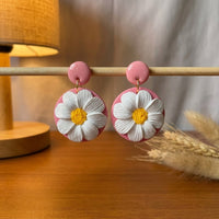 Daisy Lover handmade polymer-clay earrings, displayed on a stand in warm evening light
