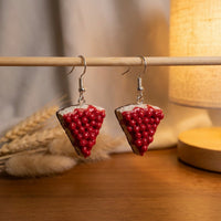 Cherry Cheesecake handmade polymer-clay earrings, displayed on a stand in warm evening light