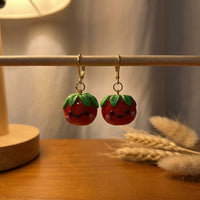 Tomatoes handmade polymer-clay earrings, displayed on a stand in warm evening light
