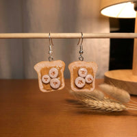 Peanut Butter and Banana earrings handmade polymer-clay earrings, displayed on a stand in warm evening light
