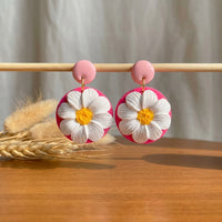 Daisy Lover handmade polymer-clay earrings, displayed on a stand in soft daylight