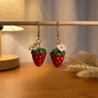 Strawberries handmade polymer-clay earrings, displayed on a stand in warm evening light