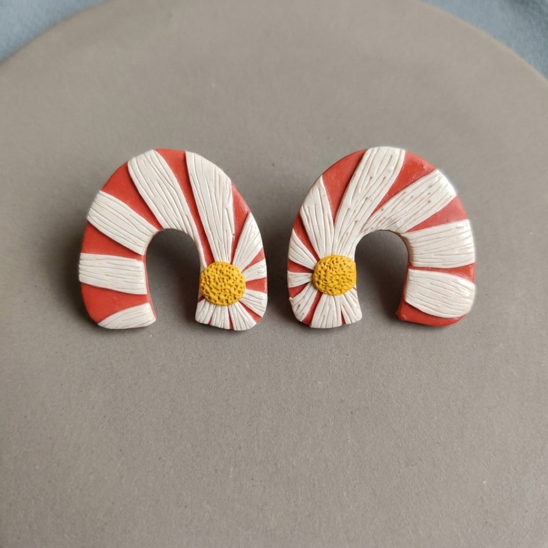 Daisy Bend handmade polymer-clay earrings, the pair on a warm stone surface