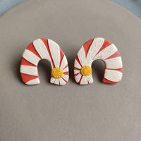 Daisy Bend handmade polymer-clay earrings, the pair on a warm stone surface