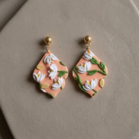 Sunset Bouquet handmade polymer-clay earrings, the pair on a warm stone surface