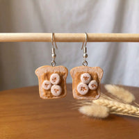 Peanut Butter and Banana earrings handmade polymer-clay earrings, displayed on a stand in soft daylight