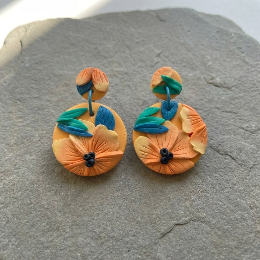 Tropical Daylily handmade polymer-clay earrings, the pair on a warm stone surface