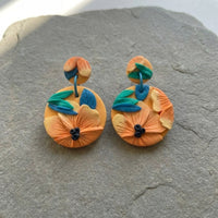 Tropical Daylily handmade polymer-clay earrings, the pair on a warm stone surface