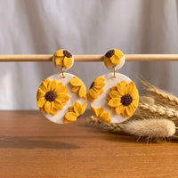 Sunflower Dangles handmade polymer-clay earrings, displayed on a stand in soft daylight