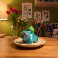 Seed Dinosaur handmade glossy clay desk pal, in the Moon Kiln studio, evening lamp light