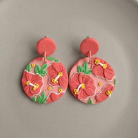 Hibiscus handmade polymer-clay earrings, the pair on a warm stone surface