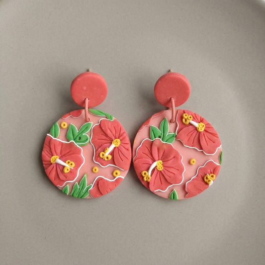 Hibiscus handmade polymer-clay earrings, the pair on a warm stone surface