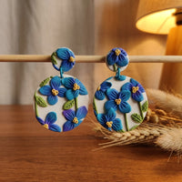 Himalayan Poppies handmade polymer-clay earrings, displayed on a stand in warm evening light